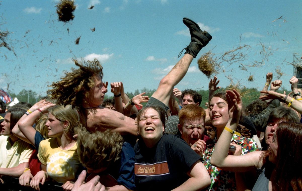 Fans crowd-surfing and singing together at an outdoor punk show.