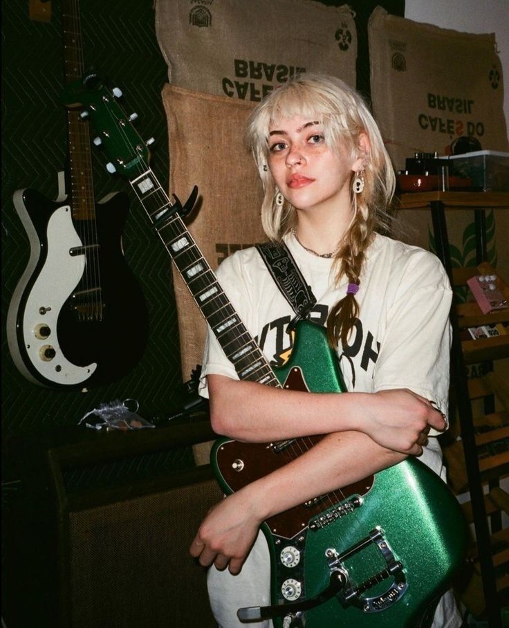 Emma character reference: a young woman holding a green electric guitar.