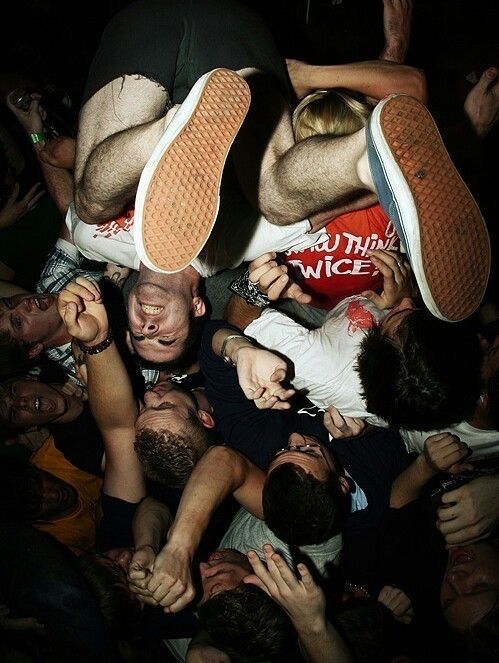 Two crowd-surfers lifted upside down by their friends at a packed show.
