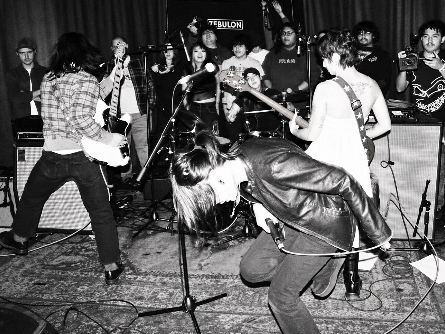 A black-and-white photograph of a punk band performing among the crowd at a small venue.