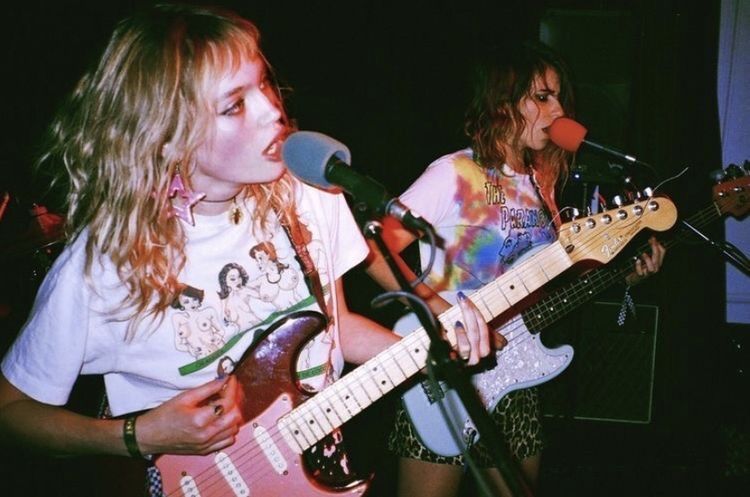 Two musicians singing and playing guitar in a small room.