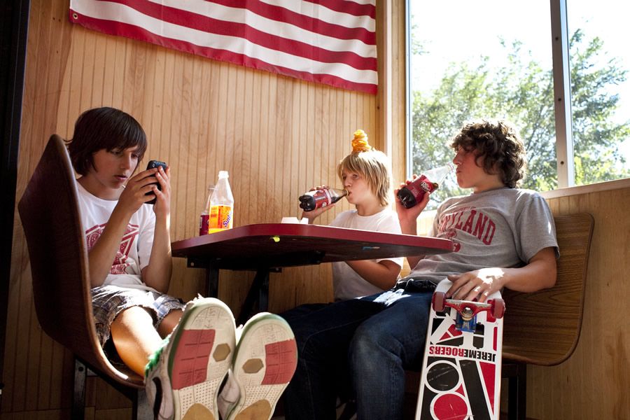 Three skaters sharing a sunny diner booth with boards and drinks.