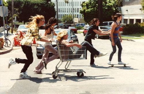Friends with a shopping cart and skateboard on a sunny California street.